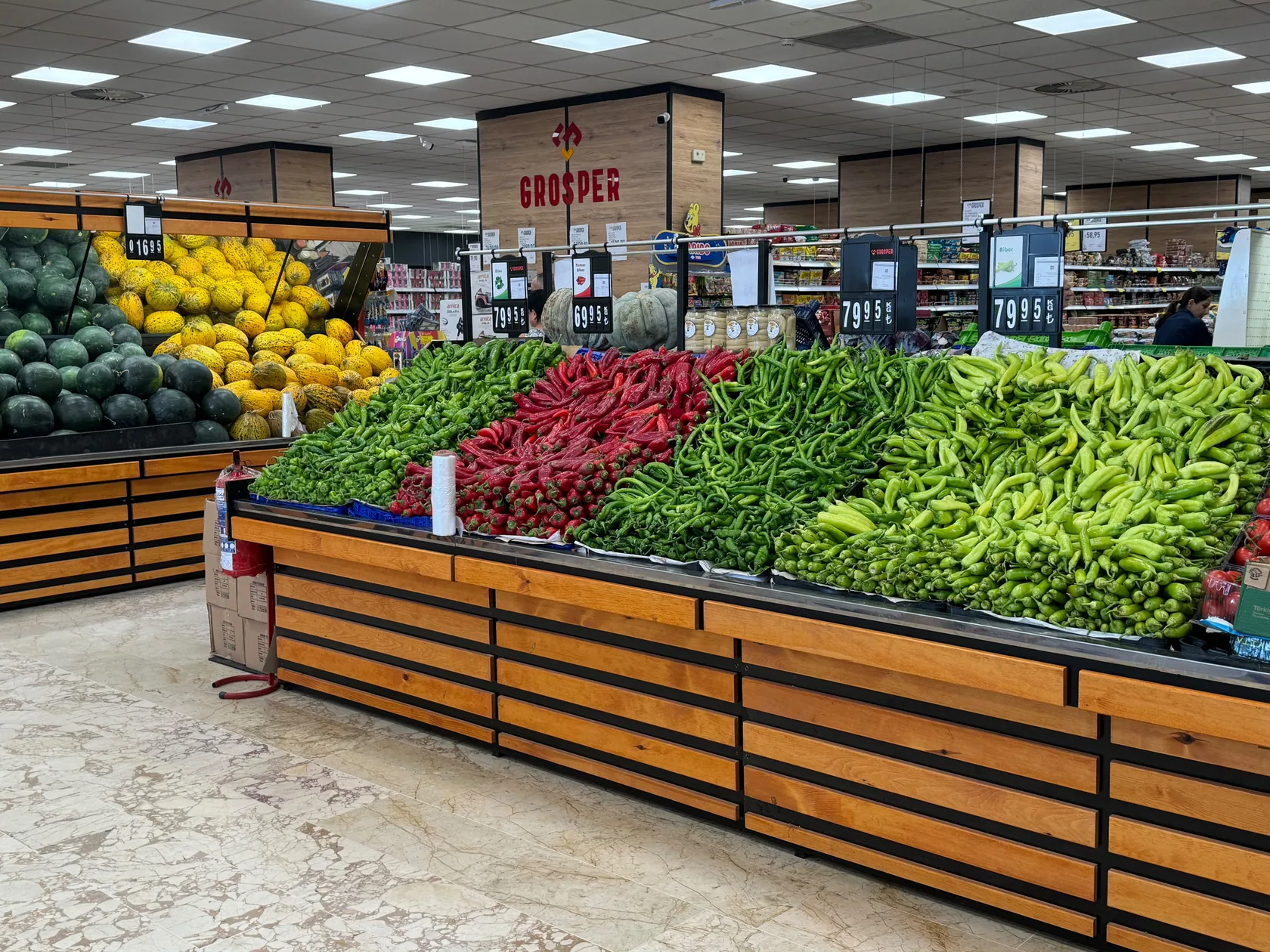 Grosper Süpermarket mağazasında ahşap kaplamalı ve koyu metal çerçeveli geniş sebze teşhir reyonu; tamamlanmış Hisar Reyon uygulaması